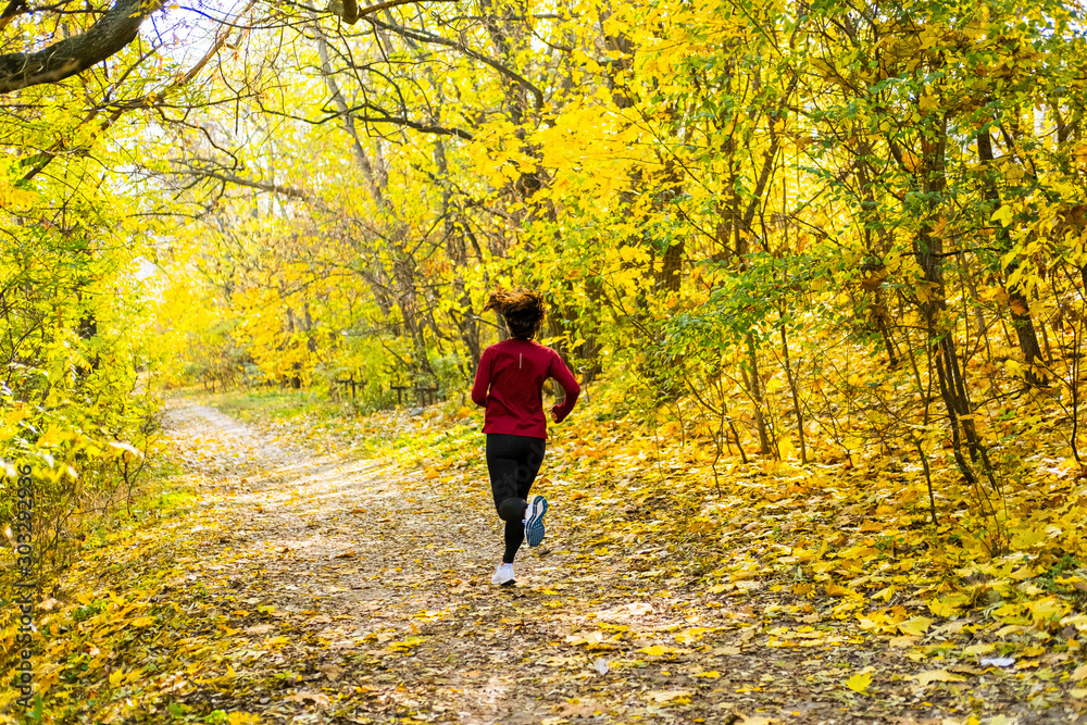 Young happy woman runner training in sunny autumn park