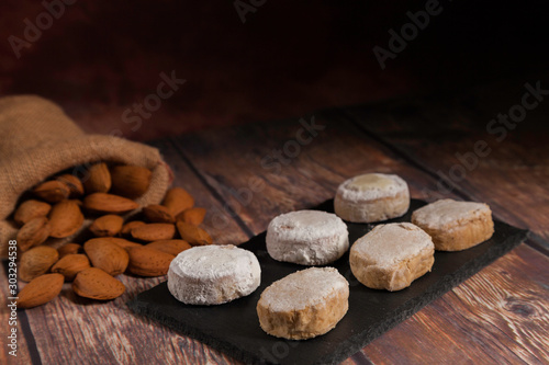 Christmas polvorones on slate plate and almond sack on wooden tableand dark background