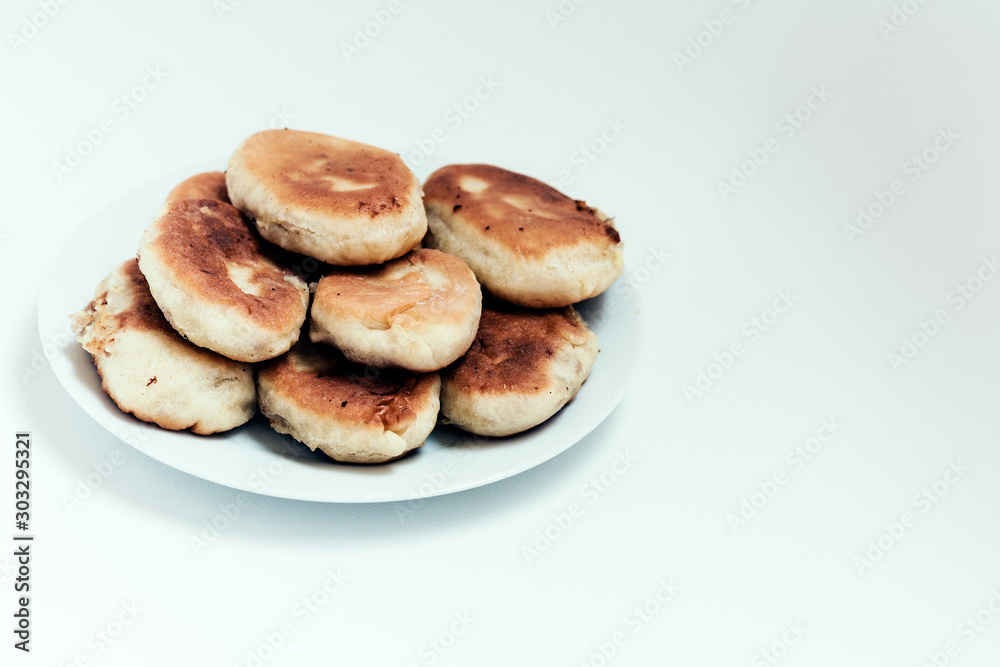 Traditional homemade fried patties or pies made of yeast dough in a rustic style on white plate.
