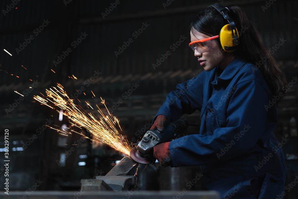 Young diverse female engineer using angle grinder in factory