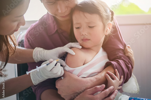 Little child having Injection,Close-up Doctor injecting vaccination to arm of asian little girl ,with the father hug the child, for not wriggle while injecting of vaccination photo