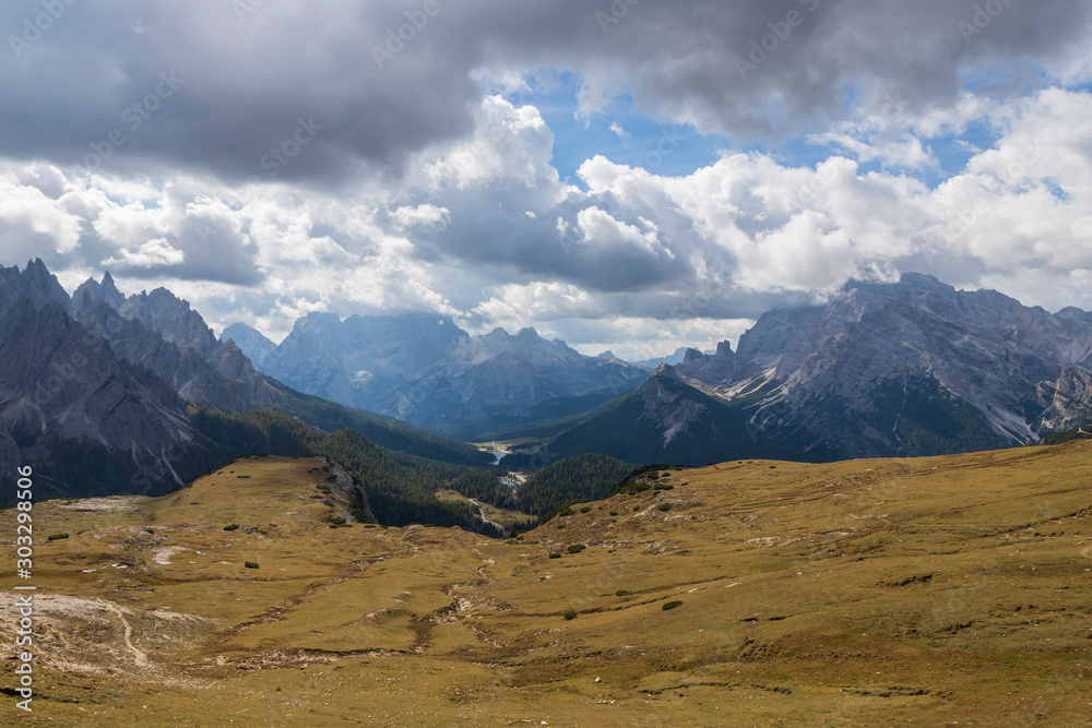 View of the mountains and valleys around Tre Cime in the Italian Dolomites. The photo has a nice background with blue sky and white clouds.