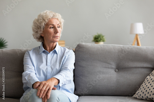 Pensive senior grandma looking away thinking of loneliness on couch