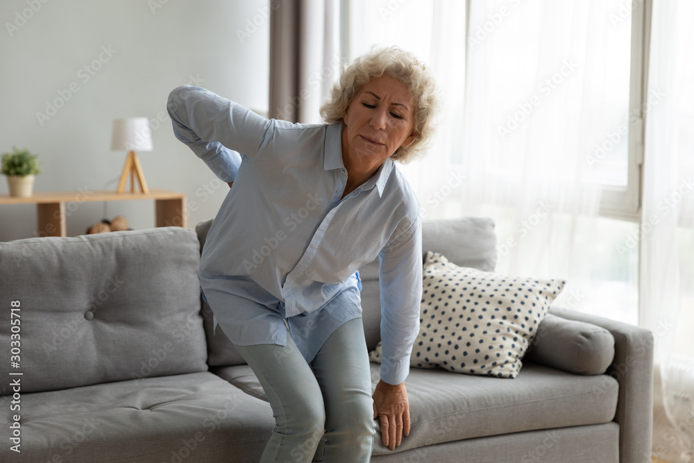 Old lady touching back feel ache getting up from sofa Old lady touching back feel ache getting up from sofa