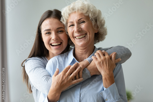 Cheerful affectionate two age generation women embracing indoors, family portrait