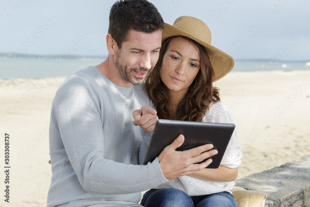 couple looking at tablet by the sea