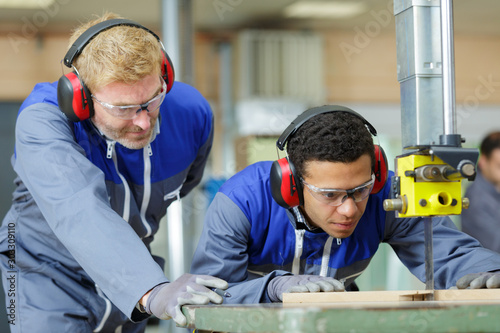 trainee carpenter using band saw under supervision