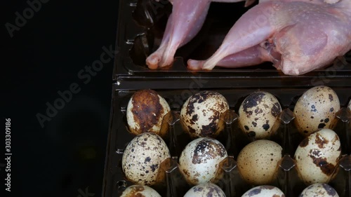 Fresh meat of quail in a plastic brown tray next to the quail eggs on a black background rotate photo