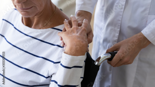 Female nurse carer supporting senior grandma on wheelchair, close up