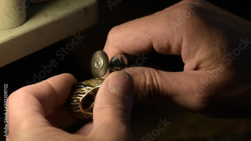 A jeweler is grinding a gold ring decorated with precious stones.
