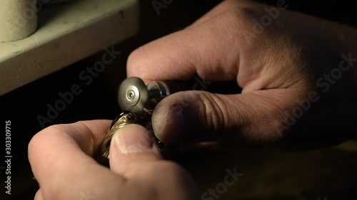 A jeweler is grinding a gold ring decorated with precious stones.