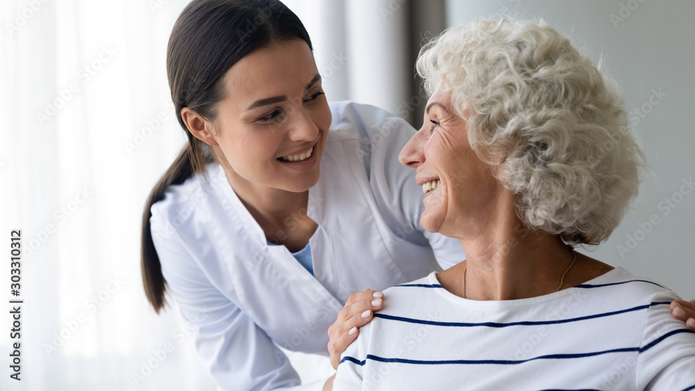 Fototapeta premium Caring smiling young nurse taking care of elder grandma patient
