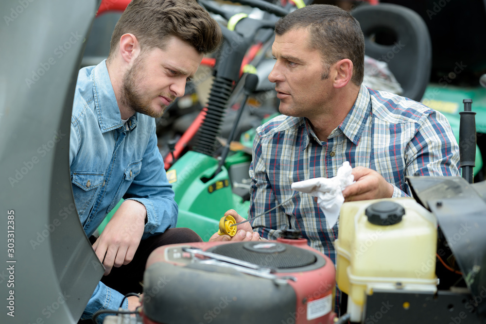 man with apprentice checking oil in lawn mower man with apprentice checking oil in lawn mower