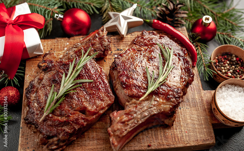 Christmas dinner for two, grilled beef steak ribeye, herbs and spices on a stone table with a Christmas tree and New Year's toys