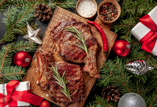 Christmas dinner for two, grilled beef steak ribeye, herbs and spices on a stone table with a Christmas tree and New Year's toys