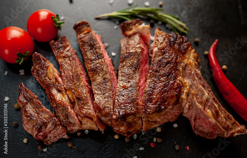 Sliced ​​grilled beef steak with spices on a stone background with copy space