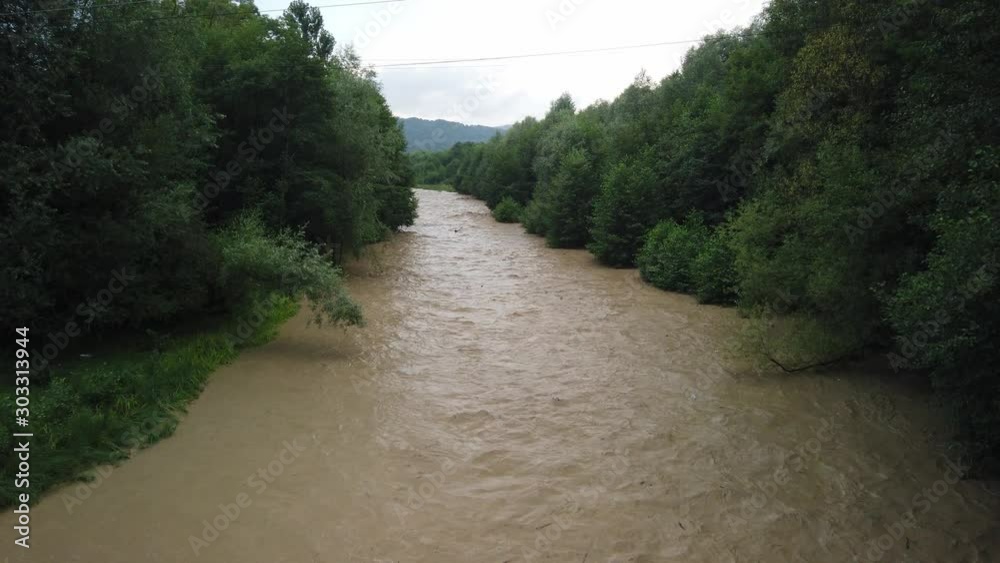 Stirred river taking its way through the trees, after a powerful storm. Muddy water in the river, flooding in summer season Stirred river taking its way through the trees, after a powerful storm. Muddy water in the river, flooding in summer season