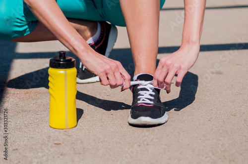 Fit woman tying her laces before a run. Female runner tying her shoelaces while training outdoor on a road. Unrecognizable young runner tying her shoelaces