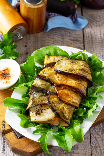Tasty fish baked with vegetables in eggplant, served with paprika yogurt sauce on a wooden table.