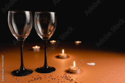Holiday background. Two clinking wine glasses, candle, confetti on orange and black background. Minimal style and valentines day concept. Flat lay, copy space