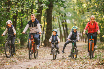 parents and kids cycling on forest trail. Young family in warm clothes cycling in autumn park. Family mountain biking on forest. Theme family active sports outdoor recreation.