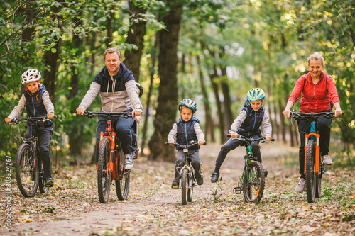 parents and kids cycling on forest trail. Young family in warm clothes cycling in autumn park. Family mountain biking on forest. Theme family active sports outdoor recreation.