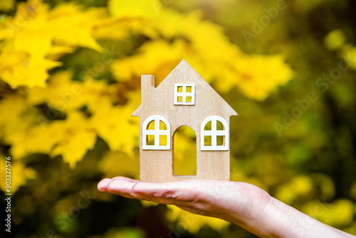 The symbol of the house in the girl's hand on the background of yellow maple leaves
