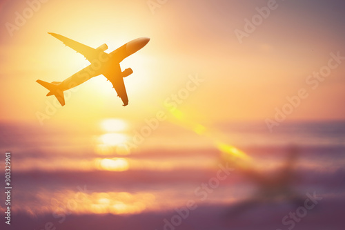 Airplane flying over tropical beach with smooth wave and sunset sky abstract background.