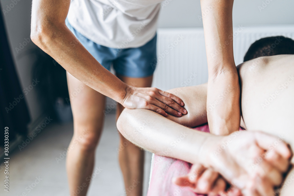 A woman physiotherapist doing back massage for a man in the medical office. Closeup of warm-up of the patient's hand