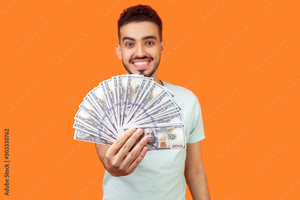 Φωτογραφία Portrait of glad positive brunette man with beard in white t-shirt holding out dollar bills at camera, offering lots of money, earning concept