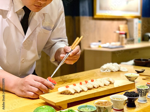 	 Closeup of chef hands preparing japanese food. Japanese Omakase Chef making sushi at restaurant. chef serving traditional japanese sushi with gold served on a stone plate.
