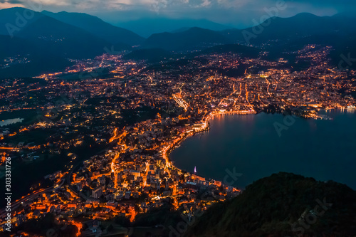 High angle aerial drone night shot of city street lights by lake in Lugano, Switzerland