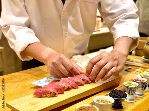  Closeup of chef hands preparing japanese food. Japanese Omakase Chef making sushi at restaurant. chef serving traditional japanese sushi with gold served on a stone plate.