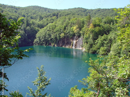Top view of a quiet azure lake surface surrounded by a mountain forest that densely covers its shores.