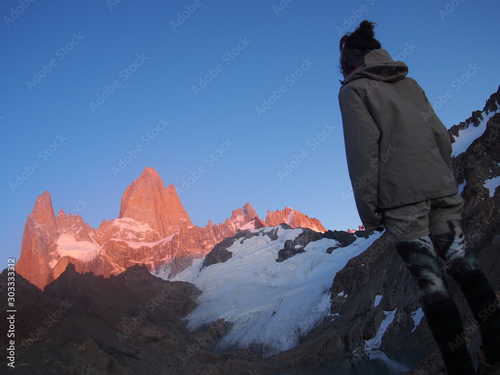 A woman hiker gazing at Mount Fitz Roy tinted red by the sunrise, Precious scenery created by nature, Los Glaciares National Park near El Chalten, Patagonia, Argentina A woman hiker gazing at Mount Fitz Roy tinted red by the sunrise, Precious scenery created by nature, Los Glaciares National Park near El Chalten, Patagonia, Argentina