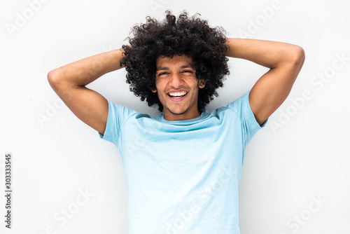 handsome young man with afro hair smiling with hands behind head against white background