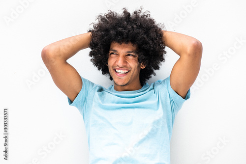 handsome young man with afro hair smiling and looking away with hands behind head against white background
