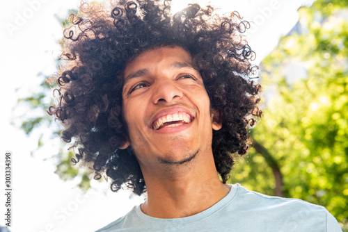 Close up handsome young North African man with afro hair smiling outside