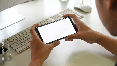 Man's hand holding smartphone with blank screen in his office. Blank screen mobile phone for graphic display montage.