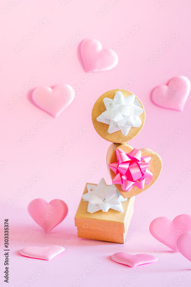 Pink gift boxes with white and pink bows are standing on top of each other on a pink background with silk pink hearts. Holiday concept.
