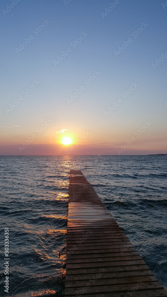 Obraz premium Bridge into the sea at sunset. sunset pier with clouds in the sea.