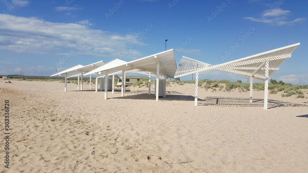 Early morning on a sandy beach without people. Sun loungers for sunbathing on the sea beach. sun loungers, summer, sunshade, beach, deck chairs Early morning on a sandy beach without people. Sun loungers for sunbathing on the sea beach. sun loungers, summer, sunshade, beach, deck chairs
