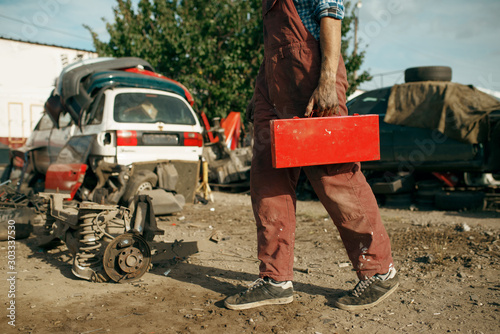 Male repairman holds toolbox on car scrapyard