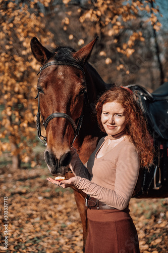 Portrait of beautiful red haired woman with horse outdoors. © Alona