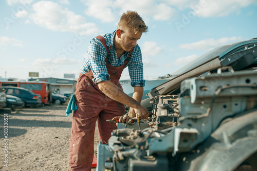 Photos Male mechanic unscrew engine on car junkyard