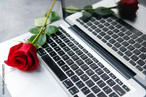 rose flower lies on the silver keyboard of the laptop and is reflected in the monitor © Elena