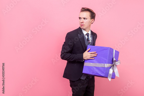 Leinwand Poster I won't share! Portrait of resentful greedy man in suit with stylish haircut holding big wrapped present and looking around cautiously, doesn't want to share gift