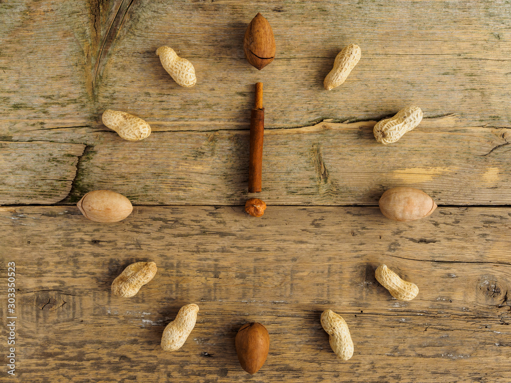 Clock made of different nuts and cinnamon on wooden background. The clock strikes twelve. New year of proper nutrition