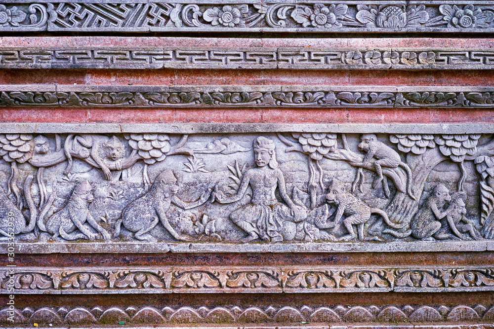 Red-grey wall texture with flowers, trees, people and animals carved on it.