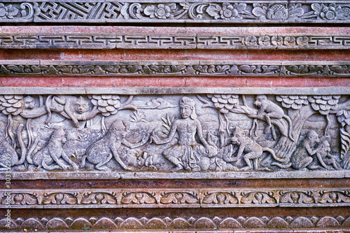 Red-grey wall texture with flowers, trees, people and animals carved on it.